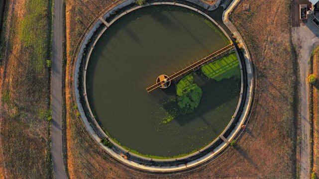 Aerial view of circular industrial water treatment tank with green algae and metal bridge structure in Rome, Lazio, Italy.