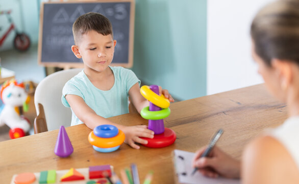 Boy sits at table and builds pyramid out of plastic toy cups. Childs behavior as marker of mental and mental health and development. Developing and maintaining skills for children with special needs