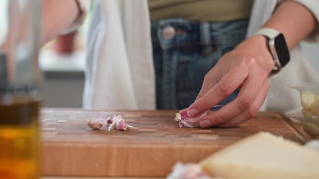 Woman peels garlic clove with knife over wooden cutting board in kitchen