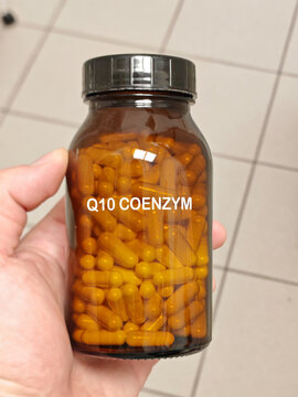Q10 COENZYM hard capsule coenzyme Q10 antioxidant supplement for cellular energy and cardiovascular health in amber glass bottle held by a pharmacist