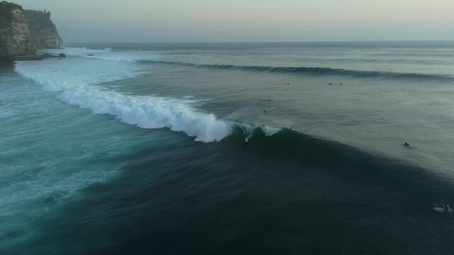 Aerial view of surfers riding waves near the cliffs of Uluwatu in South Kuta, Bali, Indonesia.