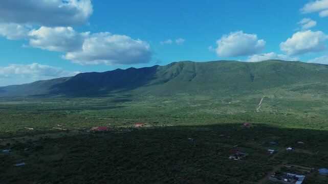Aerial view of Ngong Hills with lush green slopes, scattered rural buildings, and a bright blue sky in Kajiado County, Kenya.