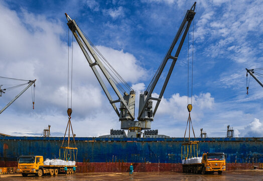 Rear view of a dock worker standing in front of a cargo ship between two trucks supervising the loading and unloading of merchandise, Indonesia