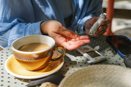 Close-up view of woman sitting at an outdoor cafe using a lancing device to test her blood glucose before drinking a cup of white coffee