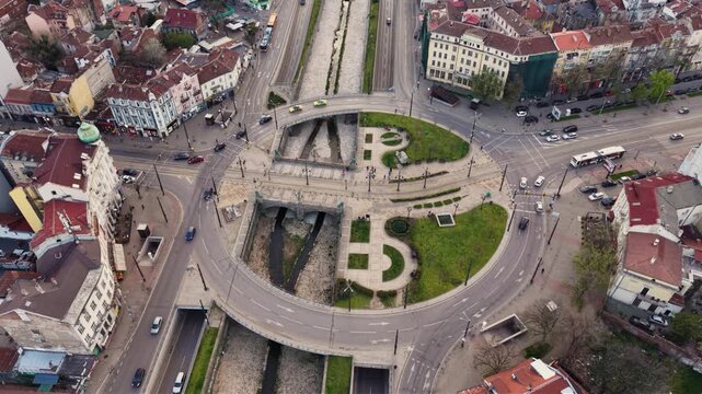 Aerial top-down view of Lions&rsquo; Bridge in Sofia, Bulgaria, showing the circular road junction, tram tracks, landscaped green spaces and the channelized Vladaya River passing beneath the historic urban 