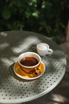 Close-up of a cup of black coffee and a small cup of milk on an outdoor cafe table on a summer day