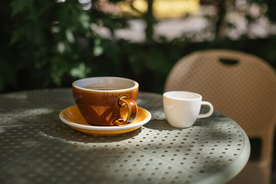 Close-up of a cup of black coffee and a small cup of milk on an outdoor cafe table on a summer day