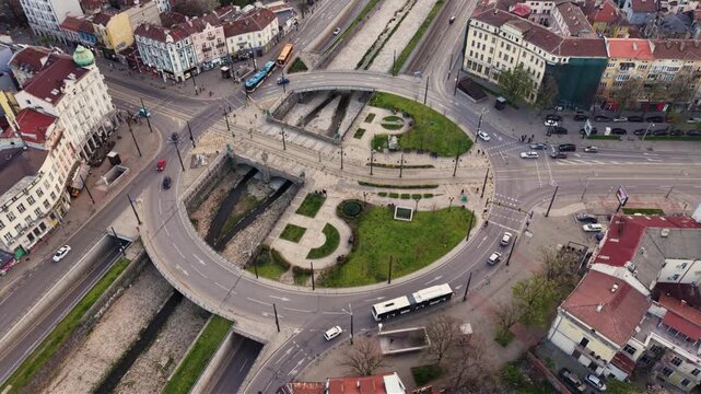Aerial top-down view of Lions&rsquo; Bridge in Sofia, Bulgaria, showing the circular road junction, tram tracks, landscaped green spaces and the channelized Vladaya River passing beneath the historic urban 