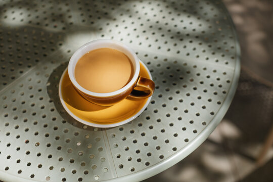 Close-up overhead view of a cup of white coffee on an outdoor cafe table on a summer day