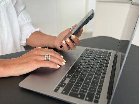 Close-up side view of a businesswoman sitting at desk with her laptop computer and using a mobile phone