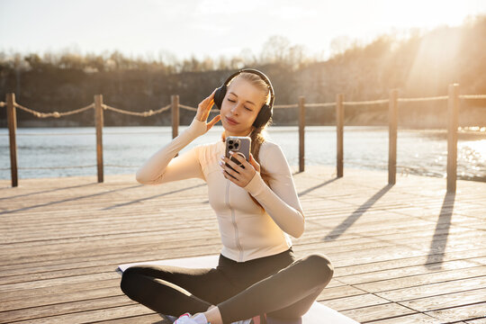 Attractive woman smiling while listening to favorite music. Beautiful woman relaxing after outdoor yoga with headphones. Healthy lifestyle concept.
