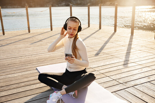 Young woman resting after fitness workout outdoors. Attractive woman listening to music with wireless headphones. Active lifestyle concept.