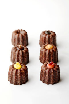 Close-up of six assorted caneles (rum cakes) with chocolate, salted caramel, lemon and raspberry cream fillings on a white background