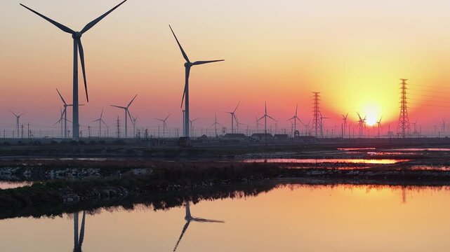 Wind turbines in a power farm reflected in paddy fields during sunset