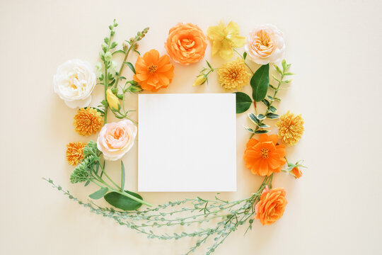 Close-up Overhead view of a blank card surrounded by assorted orange and peach garden roses, anemones and foliage