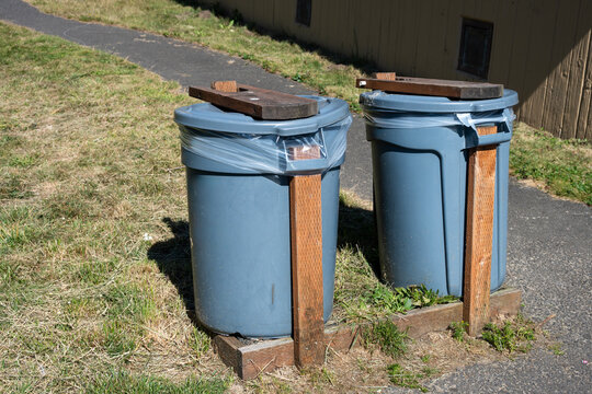 DIY, do it yourself, animal and wind proofed garbage cans, plastic trash bins reinforced with wood boards outdoors in a public park
