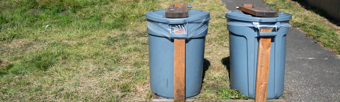 DIY, do it yourself, animal and wind proofed garbage cans, plastic trash bins reinforced with wood boards outdoors in a public park

