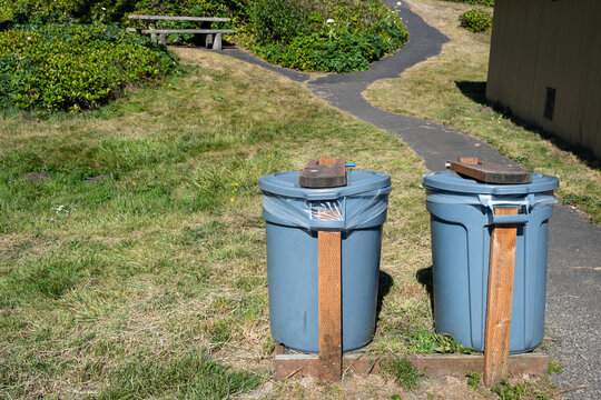 DIY, do it yourself, animal and wind proofed garbage cans, plastic trash bins reinforced with wood boards outdoors in a public park
