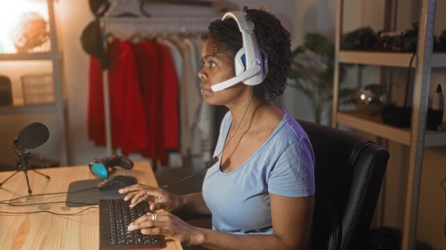 Woman gamer wearing headset with microphone, hands on keyboard beside a gamepad and mouse on desk in studio, eyes closed in pause; focused concentration.