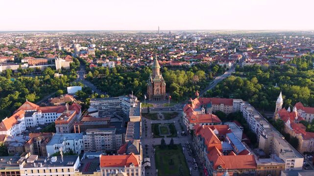 Aerial golden hour views of the Metropolitan Cathedral in Timișoara, Romania, showing its distinctive patterned roof, tall central tower and surrounding green parkland, roads and historic city neighbo