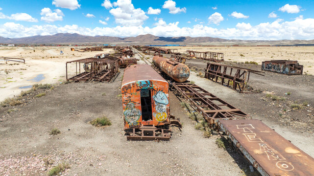 Train Cemetery featuring rusted locomotive skeletons and abandoned railway carriages scattered across the arid desert landscape. Aerial view.