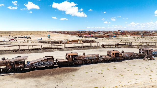 Train Cemetery featuring rusted locomotive skeletons and abandoned railway carriages scattered across the arid desert landscape. Aerial view.