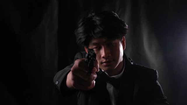 Menacing mafia hitman in a tuxedo points a smoking revolver directly at the camera in the shadows. POV concept of a dramatic assassination, organized crime execution, and cinematic thriller.

