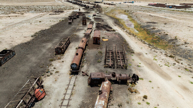 Train Cemetery featuring rusted locomotive skeletons and abandoned railway carriages scattered across the arid desert landscape. Aerial view.