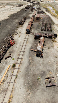 Train Cemetery featuring rusted locomotive skeletons and abandoned railway carriages scattered across the arid desert landscape. Aerial view.