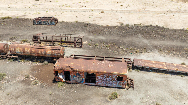 Train Cemetery featuring rusted locomotive skeletons and abandoned railway carriages scattered across the arid desert landscape. Aerial view.