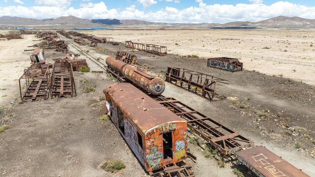 Train Cemetery featuring rusted locomotive skeletons and abandoned railway carriages scattered across the arid desert landscape. Aerial view.