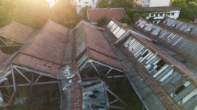 Aerial view of a severely damaged and partially collapsed industrial building roof, showing broken structural frames, deteriorated tiles and metal roofing on an abandoned factory complex.