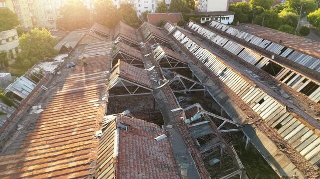 Aerial view of a severely damaged and partially collapsed industrial building roof, showing broken structural frames, deteriorated tiles and metal roofing on an abandoned factory complex.