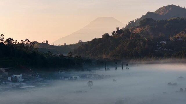 Aerial view of Dieng Plateau shrouded in morning mist with rolling mountains and golden hour light in Jawa Tengah, Indonesia.