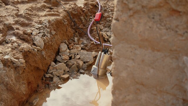 Submersible pump removing muddy water from a deep excavation trench at a construction site, with a float switch indicating water level for efficient drainage and groundwork preparation