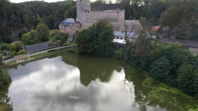 Aerial view of Kost Castle reflecting in the pond surrounded by lush greenery in Libosovice, Kralovehradecky kraj, Czechia.