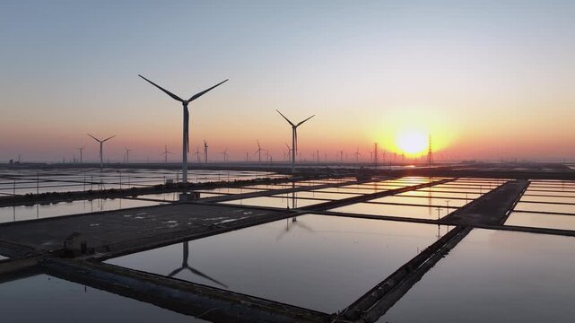 Wind turbines in salt pans at sunset with water reflections and golden sky
