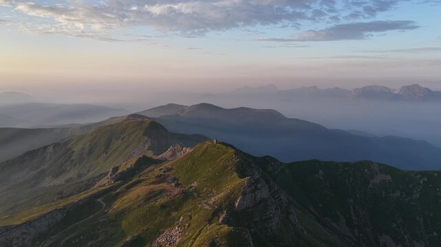 Aerial view of the mountain peaks of Cerreto Laghi at sunrise with soft light and misty valleys in the background in Cerreto Laghi, Emilia-Romagna, Italy.