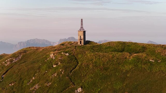 Aerial view of an old stone tower standing on a grassy mountain ridge during golden hour in Cerreto Laghi, Emilia-Romagna, Italy.
