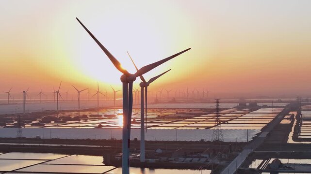 Wind farm complex at sunset over salt pans with reflective water surfaces and silhouetted turbines