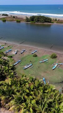 Aerial view of traditional fishing boats resting on the grassy shore near the coast in Kecamatan Kebumen, Jawa Tengah, Indonesia.