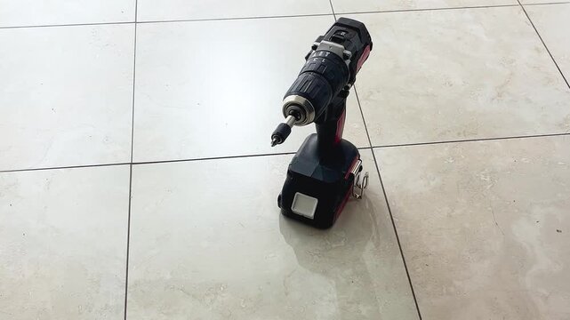 Zooming view of a professional cordless screwdriver on a tile floor representing tools for construction, home improvement and workshop tasks.