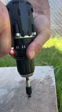 Close up view of a skilled handyman's hand using an electric cordless screwdriver to fasten a screw into a rustic wooden board, representing a construction and repair project.