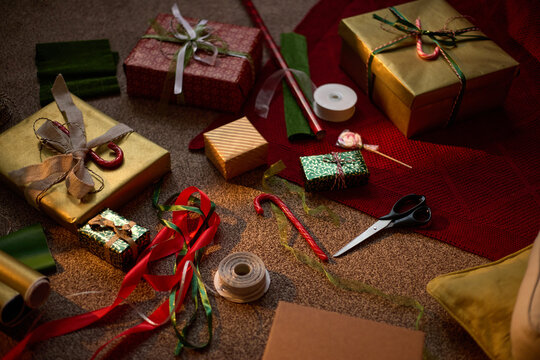 Wrapped Christmas gifts, ribbons, scissors, and wrapping paper scattered on floor, preparing holiday presents. High angle shot useful for festive marketing and seasonal retail promotions