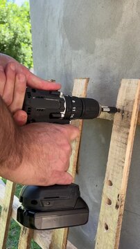 Close-up of an expert using a cordless electric screwdriver to tighten a screw into a wooden fence. Outdoor repair projects. Labor Day in the USA