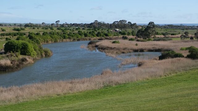 Hovells Creek meandering through open grasslands, wetlands, and dense reed beds in Lara, Victoria, Australia. Native vegetation and grassy slopes border the calm waterway