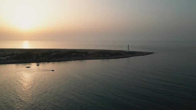 Aerial view of San Vito Lo Capo lighthouse at sunset with calm sea and small boats along the coastline in San Vito Lo Capo, Sicily, Italy.