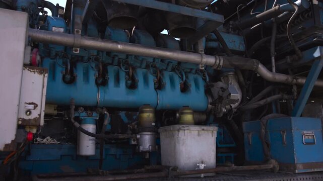 Blue industrial engine bay with twin circular fan housings, dense pipes, hoses, filters, weathered metal structure, front view in tight low-angle daylight composition