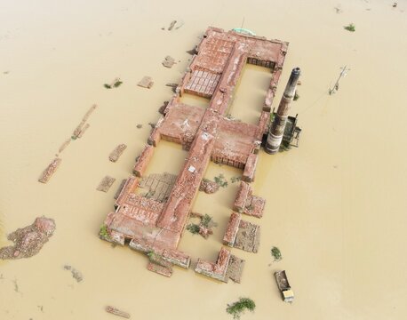 Aerial view of a flooded brick kiln structure with a tall chimney surrounded by murky brown floodwater in Chhagalnaiya, Chittagong Division, Bangladesh.