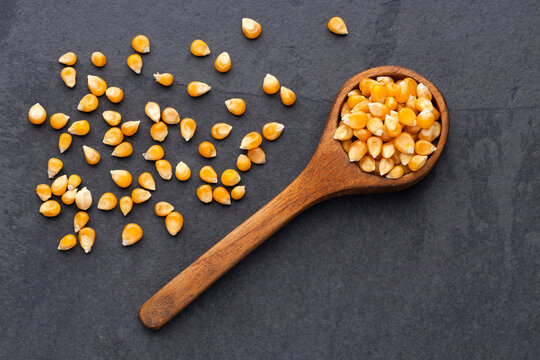 Popcorn kernels presented in a wooden spoon with scattered kernels, ideal for cooking and food concepts
